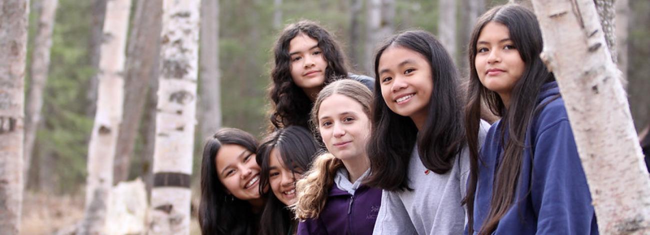 Five students smiling and sitting on log.
