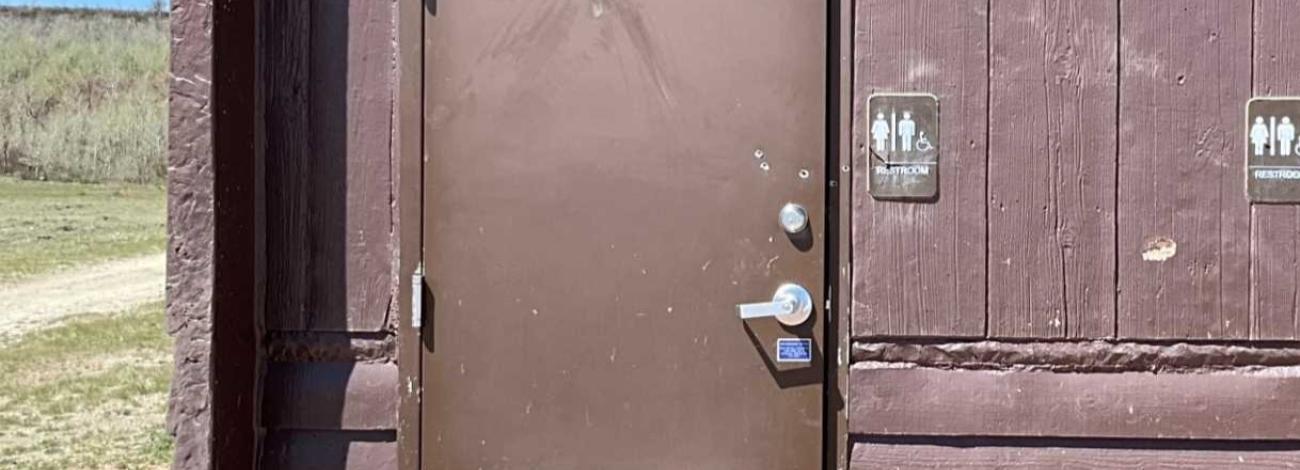 Campground vault toilet with bullet holes.