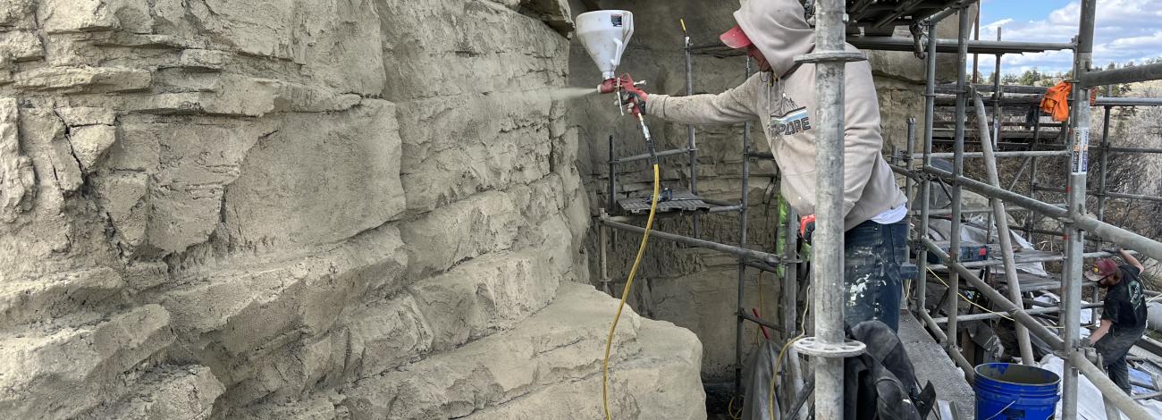 A person standing on scaffolding sprays paint onto a rock face.