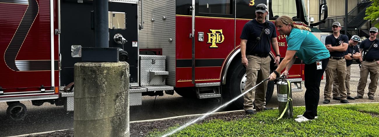 A local firefighter guides Wild Horse and Burro Compliance Specialist, Megan Velasquez, through using a fire extinguisher during a hands‑on safety demonstration.
