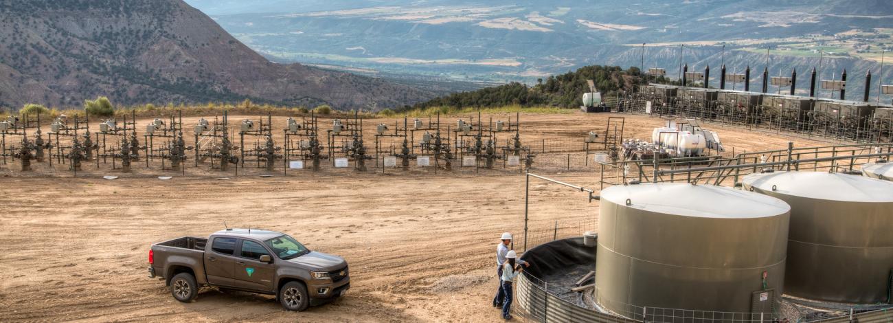 Panoramic photo of an oil and gas field in Colorado with holding tanks, a BLM pick up and other infrastructure 
