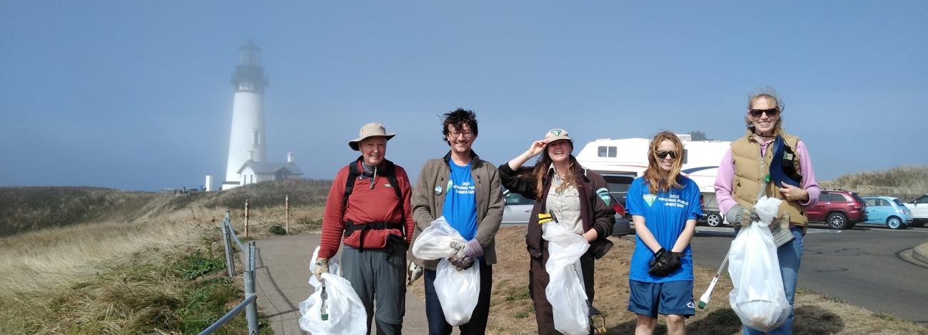 Group of people holding cleanup bags on a path near a foggy lighthouse.
