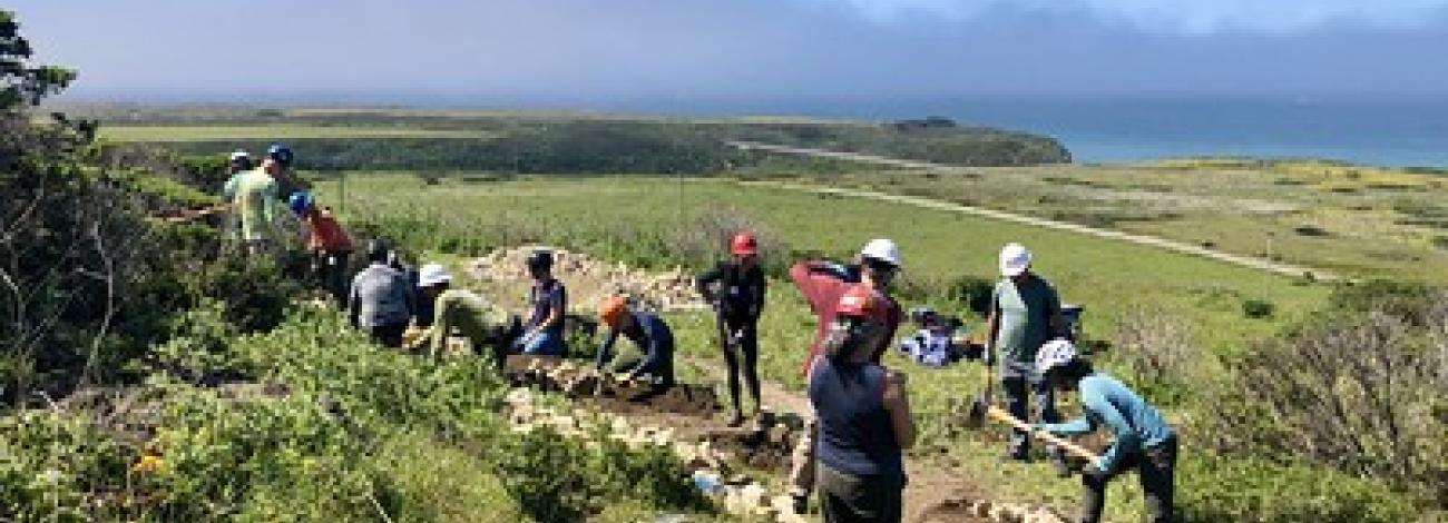 People repairing a trail overlooking the Pacific Ocean.