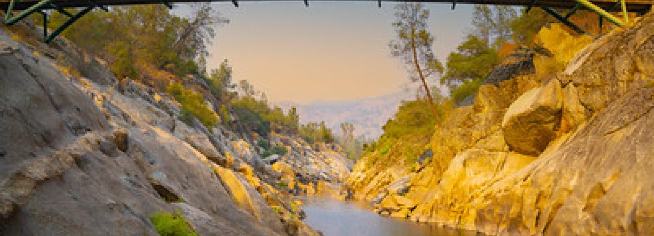 A large green bridge over a granite gorge at sunset