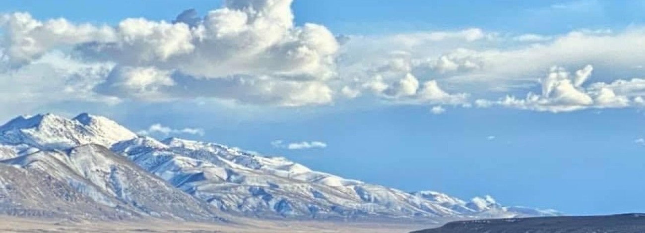 A snow covered mountain with blue sky and puffy clouds.