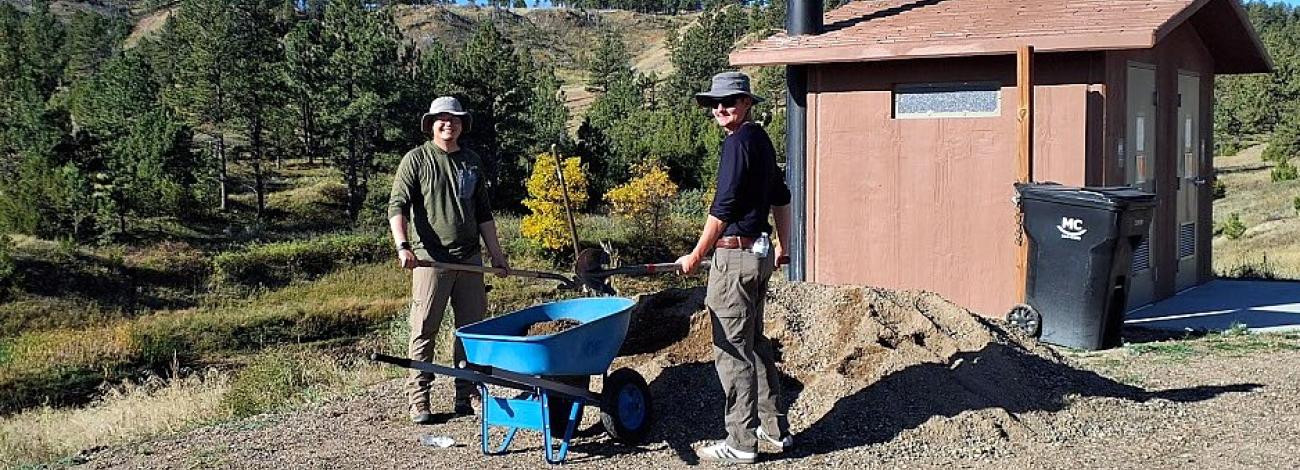 Two volunteers load a wheelbarrow from a pile of gravel