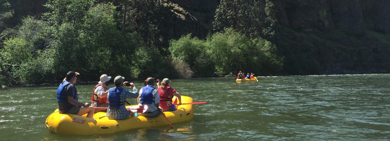 Group rafting on a river through a canyon landscape.