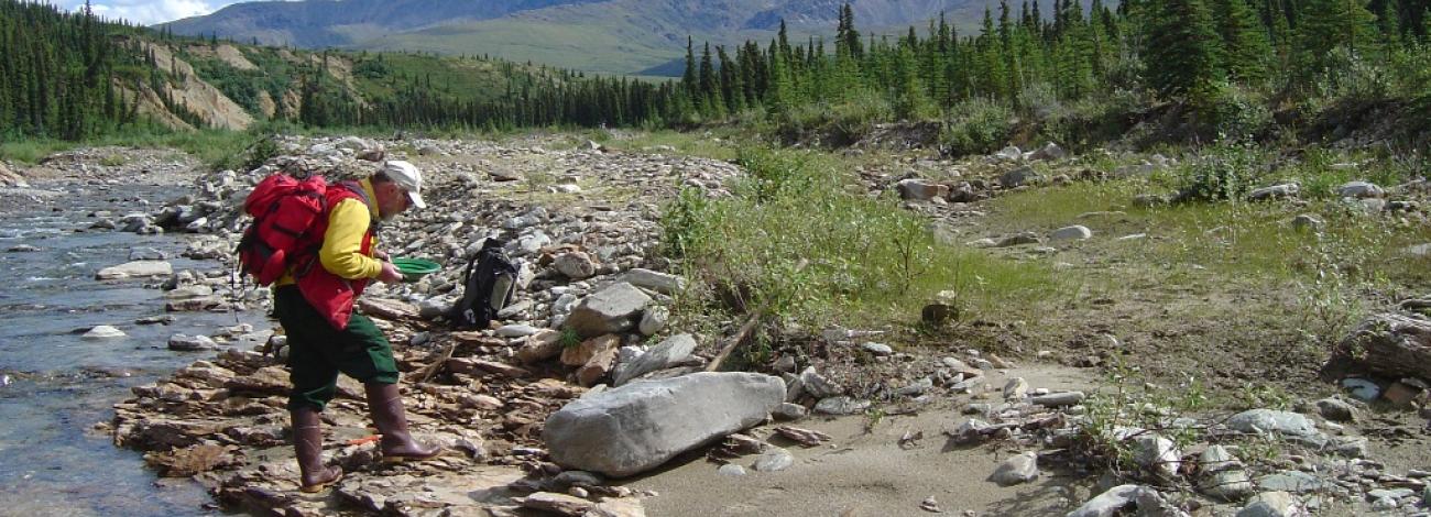 Geologist on the banks of a creek taking a closure look at a rock