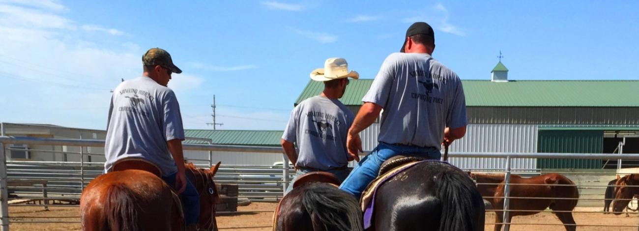 Three men riding horses at corral at Hutchinson Facility