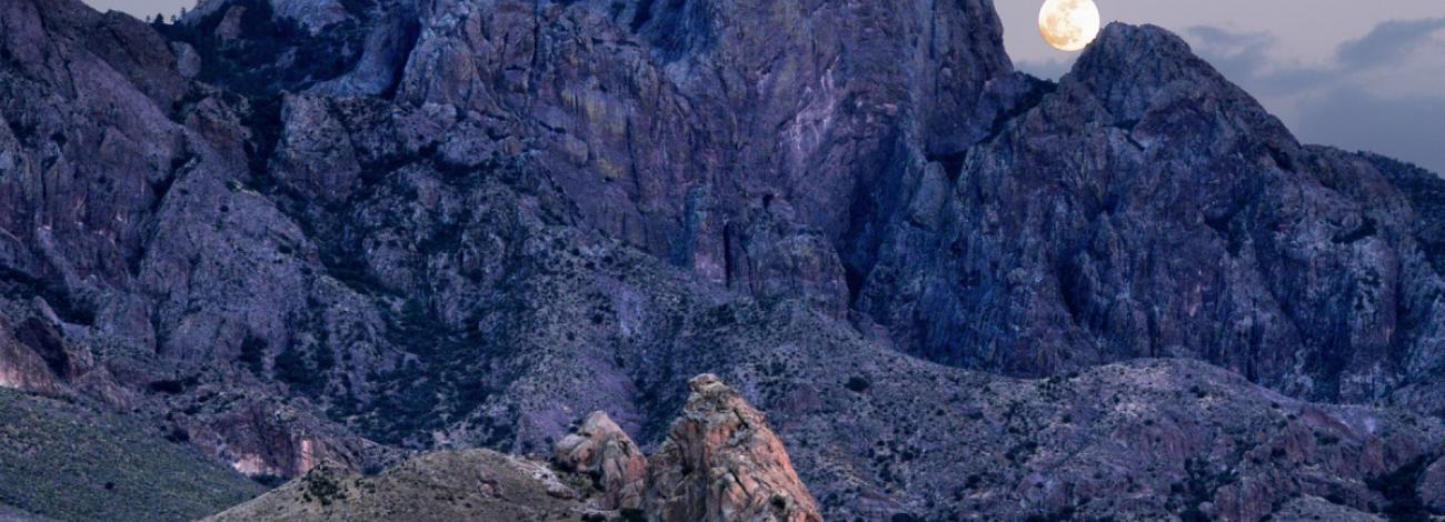 The moon peeking over the steep, angular Organ Mountain range in the Organ Mountains-Desert Peaks National Monument.