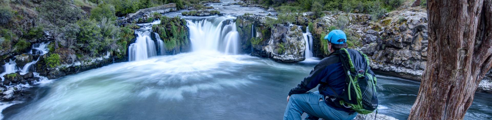 A man sits and looks at a waterfall at Arkansas River from the rocky edge of the river.