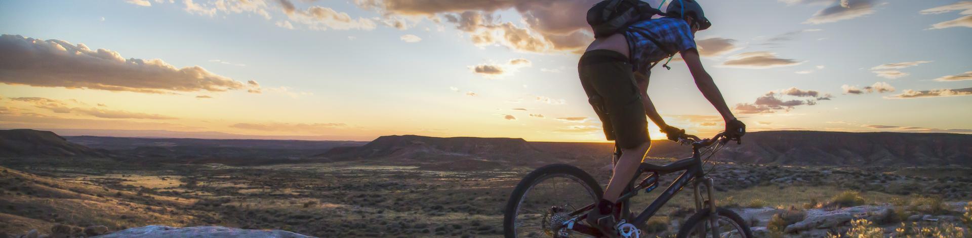 A person on a bike, rides along a trail at sunset.
