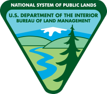 The BLM Official Logo displaying an inverted triangle with a pine tree, snow capped mountain, a river an hills.