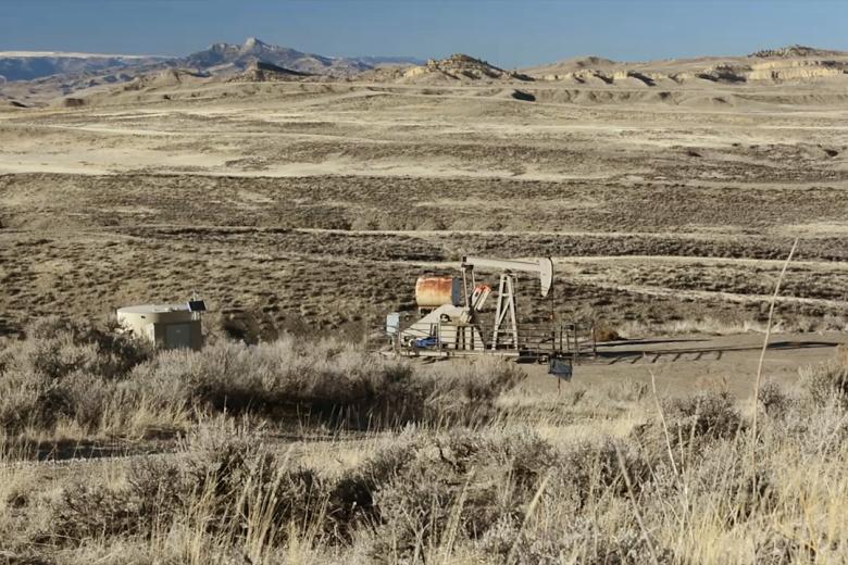 rolling Wyoming sagebrush landscape in shades of tan with a oil pump jack and tanks painted to blend.