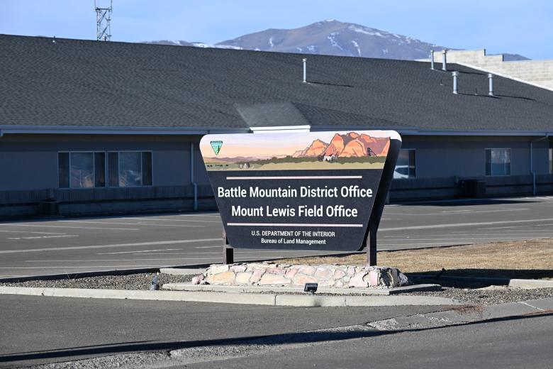 With a blue sky and snow-capped mountain in the background, a Bureau of Land Management sign sits in front of the Battle Mountain District Office which includes the Mount Lewis Field Office.