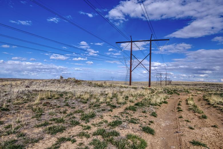 Powerline spanning across a brushy flat area with blue skies and a few white clouds in the distance.