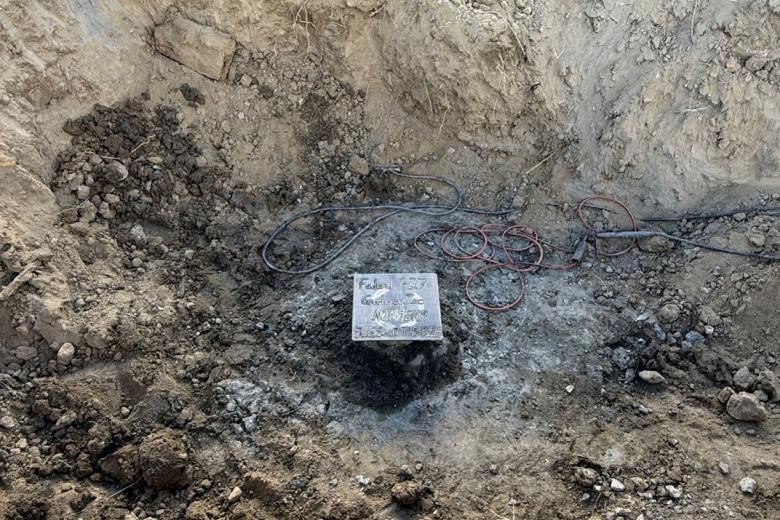 A square piece of metal with writing in the bottom of a large hole in the dirt. Various cords are coiled nearby. 