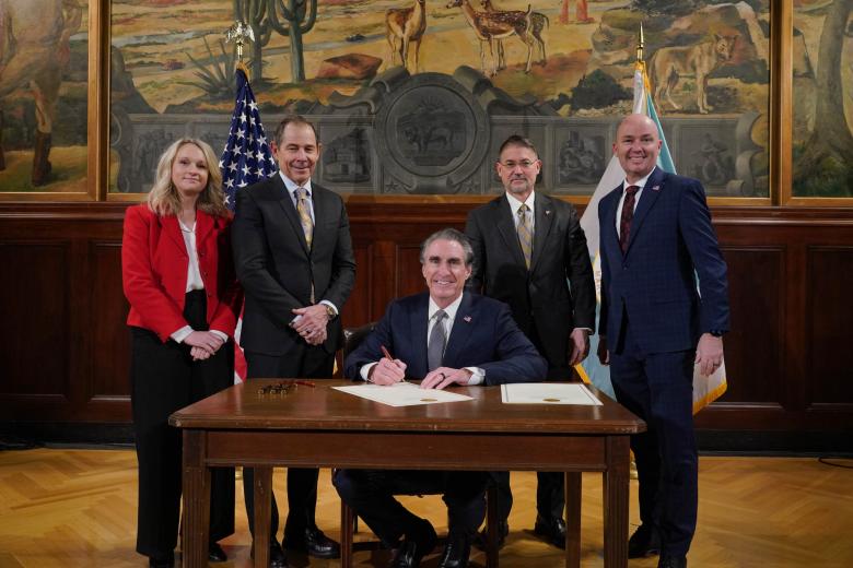 Interior Secretary Doug Burgum sits at a table and smiles after signing documents. Utah Senator John Curtis is to his right, Acting BLM Director Jon Raby and Utah Governor Spencer Cox are to Burgum's right.