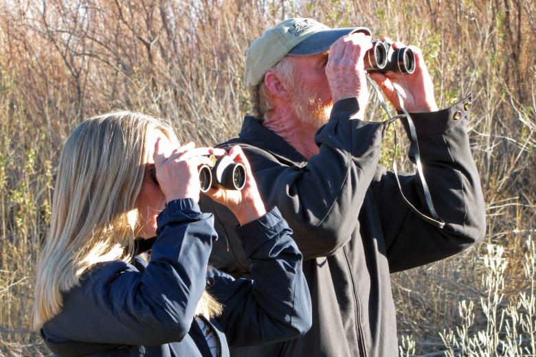 two people hold binoculars to their eyes