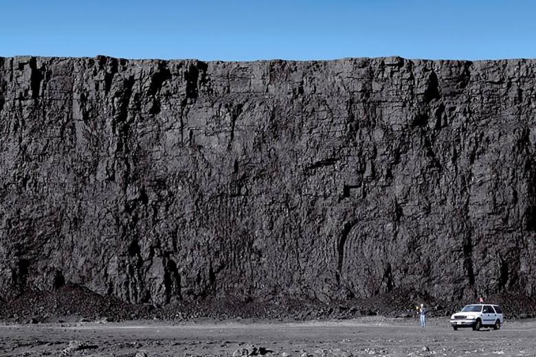 Huge coal wall at the Powder River Basin with worker wearing hardhat and truck at the base of it in Wyoming