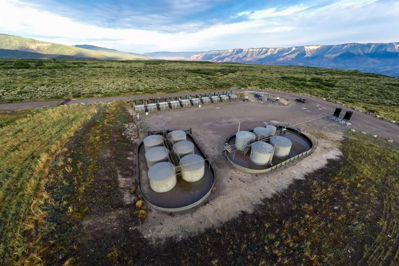 Oil and gas infrastructure including pipes, valves and tanks on a gravel pad 
