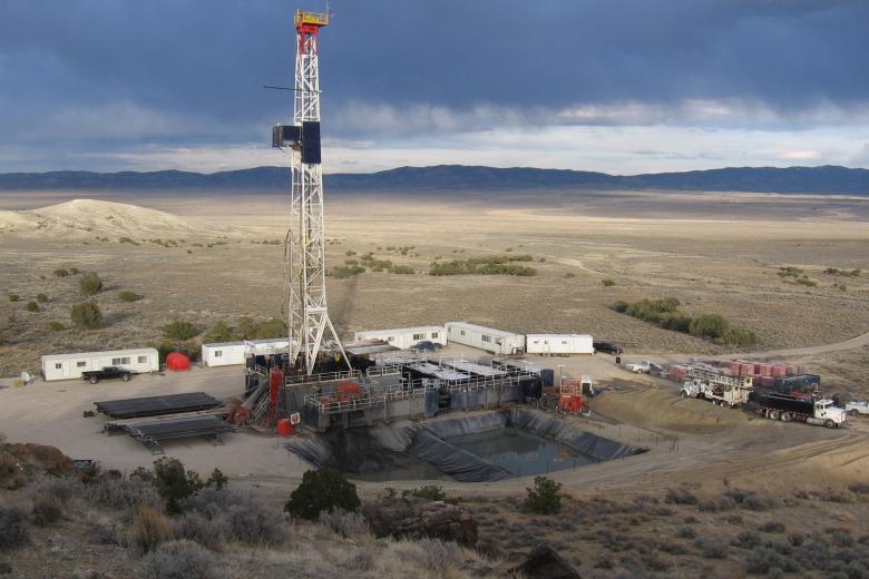 An oil and gas drill rig and pad are seen on an open plain with dark clouds overhead