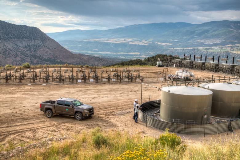 Panoramic photo of an oil and gas field in Colorado with holding tanks, a BLM pick up and other infrastructure 