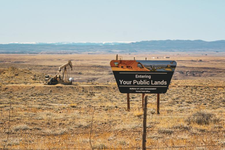 A BLM sign for the Vernal Field Office with an oil derrick in the background.