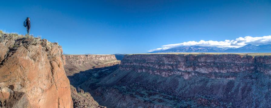 A lone hiker standing at the rim of the Rio Grande Gorge