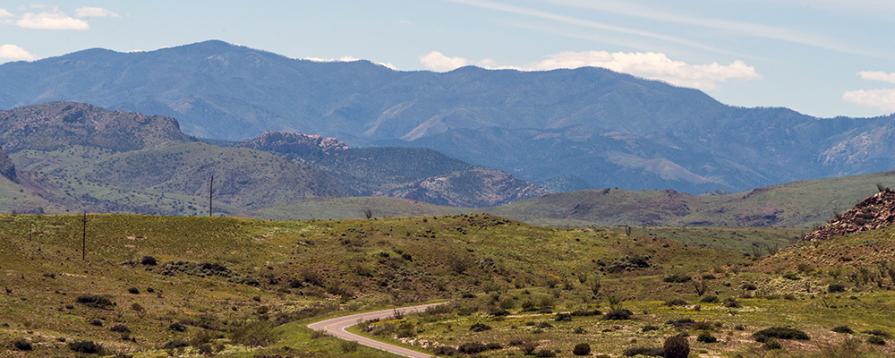 A paved road of the Lake Valley Backcountry Byway winding through low hills with larger mountains in the background