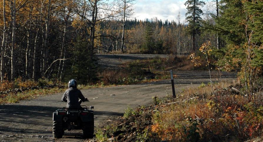 Alaska OHV rider riding four wheeler on easement approaching 17b Easement marker during fall