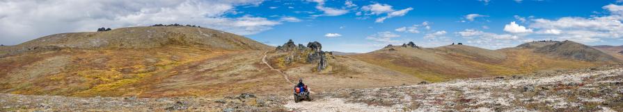 A rider on an ATV navigates a rocky trail through a treeless mountain valley.