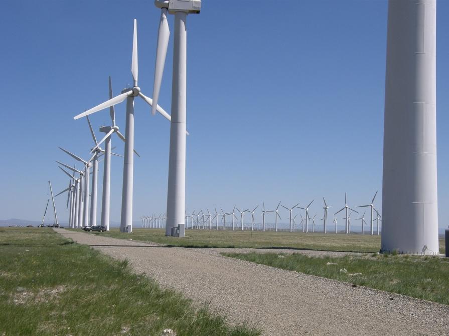 Image shows wind turbines set in a grassy field actively spinning under a clear blue sky.