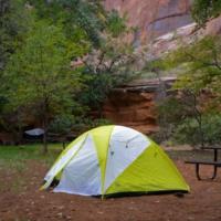 Tent at a campground site with trees and mountains in the background. 