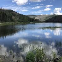 The glassy surface of Shaw Reservoir reflects the sky, clouds, and mountains that surround the lake.