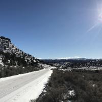 A snowy road winds through sage brush under a blue sky.