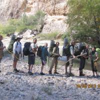 Nine people standing on the bank of a creek with some of them carrying unique fish traps on their backs