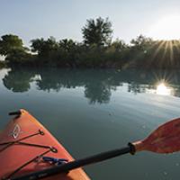 The view from a red kayak on a calm river at sunrise.