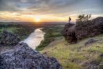 Woman standing on a rock overlooks sunset over river