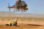 Helicopter hovering over the ground with three firefighters underneath.