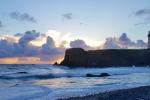 The Yaquina Head headland jutting out into the sea with the Yaquina Lighthouse on top. The sun is setting and the light is a deep blue.