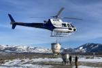 A helicopter dropping seed with two men on the ground. 