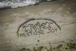 aerial view of ochre sea stars forming the words "Restore Joy" in the sand. 