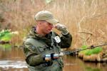 A veteran holds his fishing pole as he fishes in a stream. 