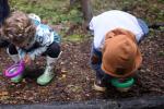 Two small children look through a magnifying glass on a nature trail outside.