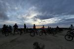 A photo of a group of youth mountain bike riders sitting atop their bikes on a desert trail, with an evening cloudy sky in the background.