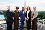 Five people standing on top of a building with the National Monument in the background. 