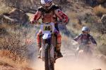 A person in full motor bike racing gear on a motorcycle driving through the desert
