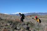 Teenager and adult firefighter hike up a hill with firefighting equipment.