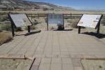 A photo showing a brick path leading to three interpretive signs for the Overland Trail in Wyoming. The signs on the left and right have written descriptions and colorful images and the sign in the middle has three Braille plaques describing the site.